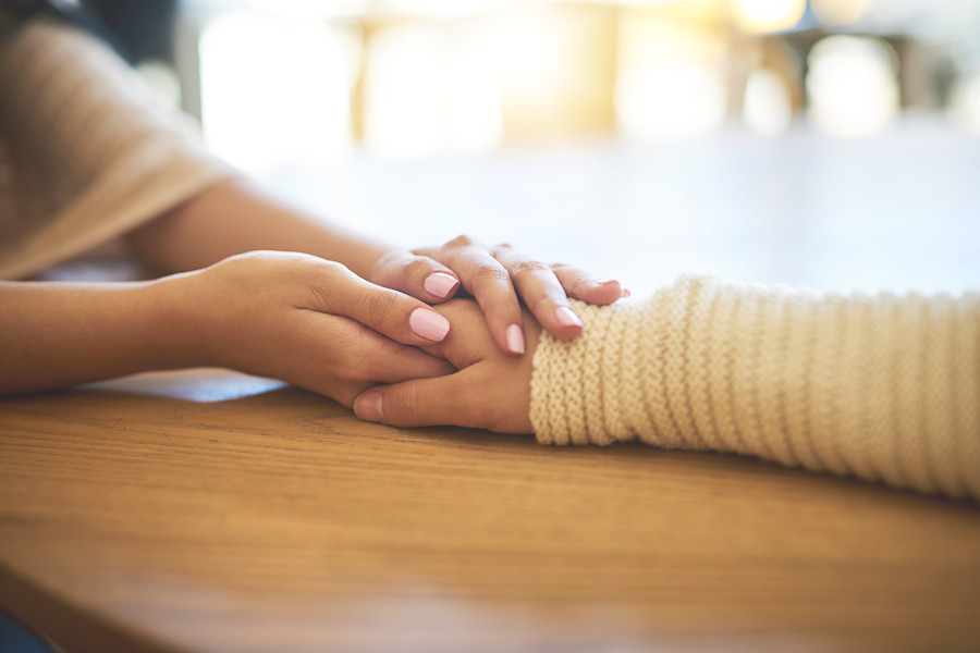 Zwei Hände legen sich schützend über eine andere Hand.