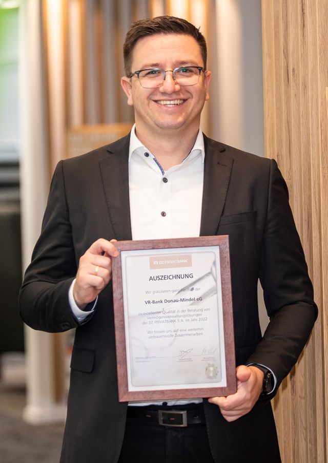 Berater Private Banking Julian Bachert mit Auszeichnung der DZ Privatbank hält einen Bilderrahmen in der Hand.