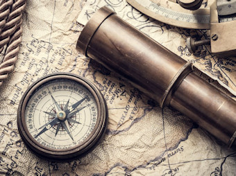 Ein altertümlicher Kompass und ein Fernrohr liegen auf einer historischen Landkarte.