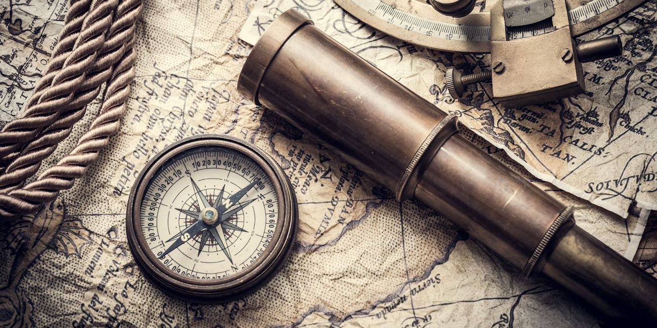 Ein altertümlicher Kompass und ein Fernrohr liegen auf einer historischen Landkarte. 