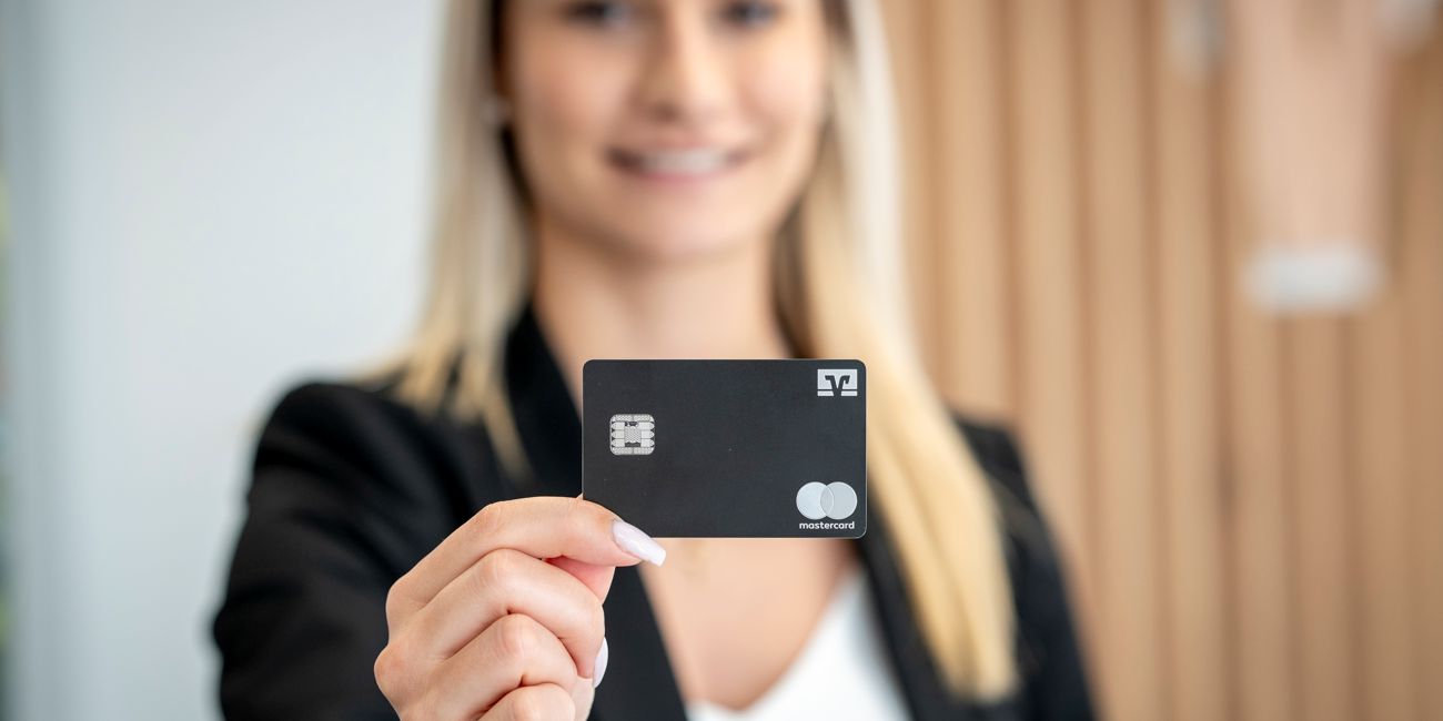 Eine Frau hält eine schwarze Kreditkarte mit VR-Bank Logo und MasterCard Logo in der Hand.