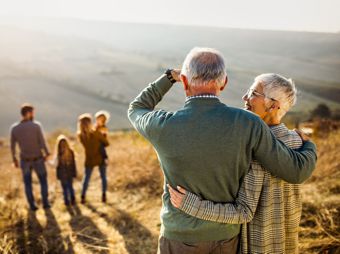 Ein älteres Ehepaar blickt über die Berge auf eine jüngere Familie mit zwei Kindern.