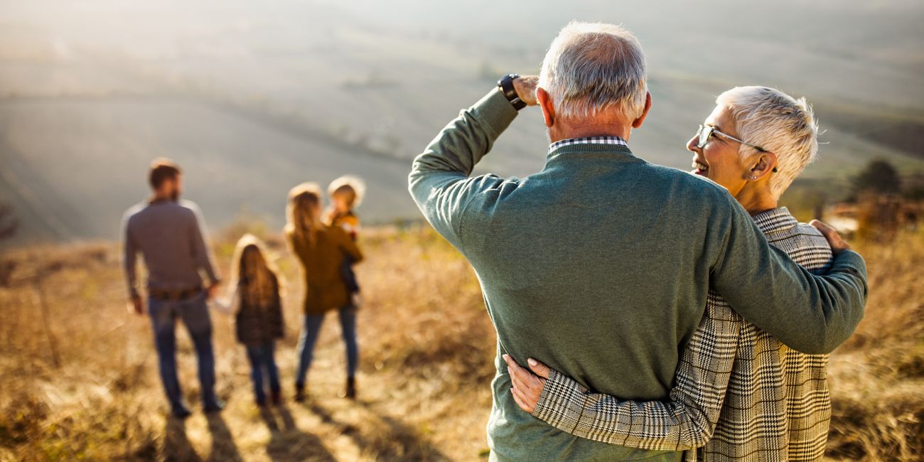 Ein älteres Ehepaar blickt über die Berge auf eine jüngere Familie mit 2 Kindern.
