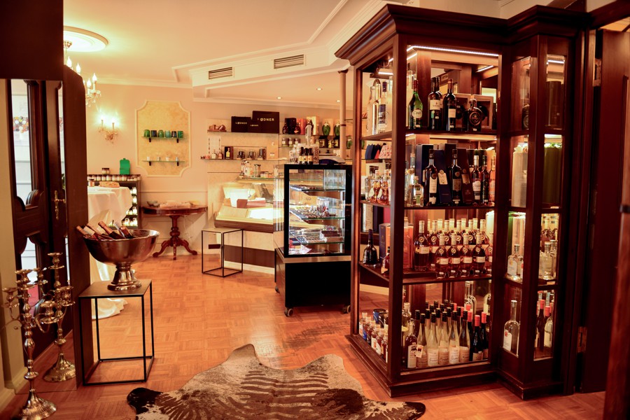 Gemütlicher Ladenbereich mit hochwertigen Spirituosen in einer Vitrine, daneben ein kleiner Kühlschrank und Regale mit Produkten.