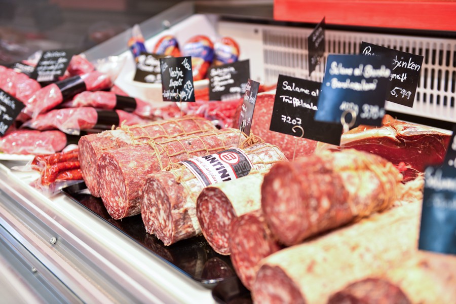 Feinkosttheke mit verschiedenen Sorten Salami und Wurst, beschriftet mit kleinen Tafeln, appetitlich angerichtet.