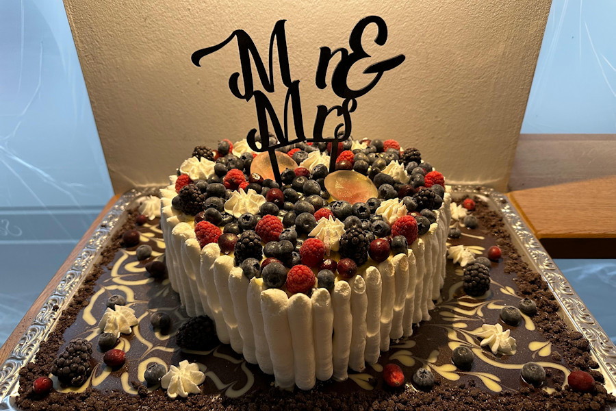 Herzförmige Eistorte zur Hochzeit auf einem Tablett mit verschiedenen Beeren und einem Mr & Mrs Tortenstecker.