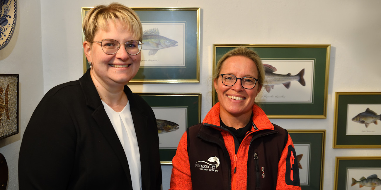 Private Banking Beraterin Martina Walburger und Isabelle Vollmann-Schipper stehen vor einer Wand, an der Bilder von Fischen hängen.