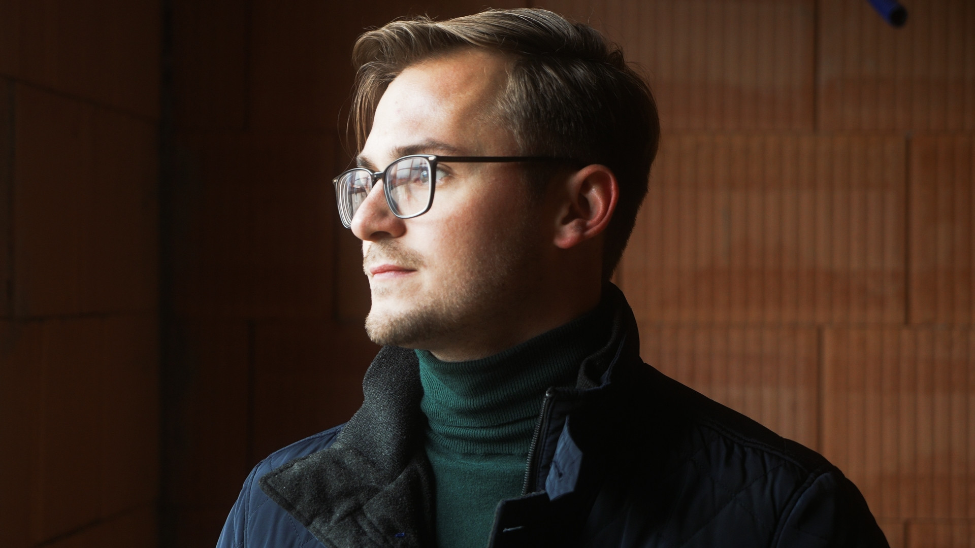 Benedikt Griener steht vor einer roten Ziegelwand.