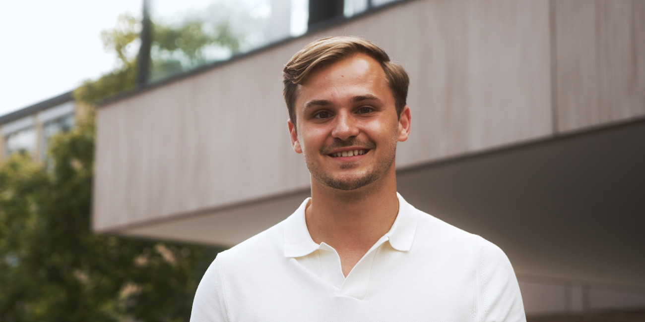 Benedikt Griener steht vor einem Gebäude und lächelt in die Kamera.