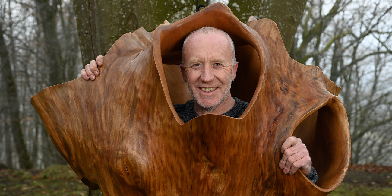 Bernhard Schmid blickt aus einem seiner Holzkunstwerke heraus.