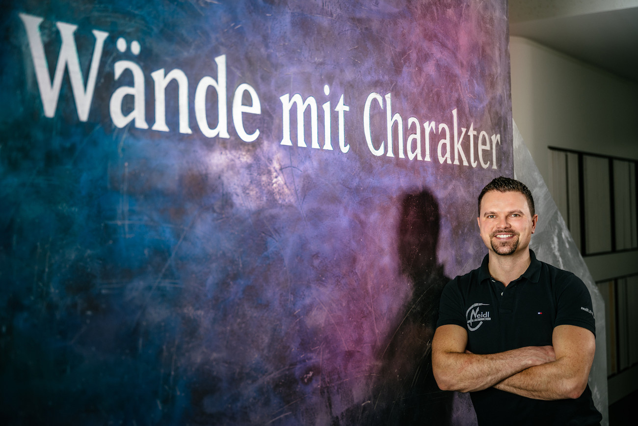 Christian Neidl vor einer blau-lila gemusterten Wand mit der Aufschrift Wände mit Charakter.