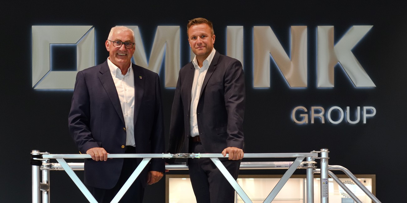 Zwei Männer im Anzug stehen vor dem MUNK Group Logo. Links: Ferdinand Munk, rechts: Jan Iffert (Bereichsleiter Private Banking). Sie lehnen sich an ein Aluminiumgerüst.