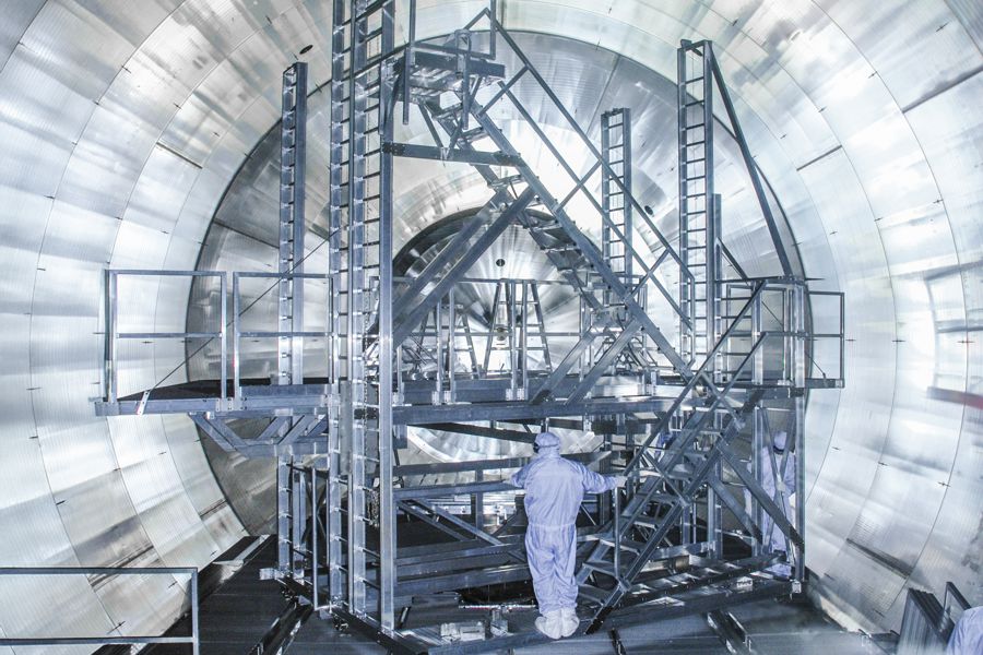 Eine große Testkammer mit komplexem Leiter- und Plattformsystem, in der ein Mitarbeiter im Schutzanzug an einer Anlage arbeitet.