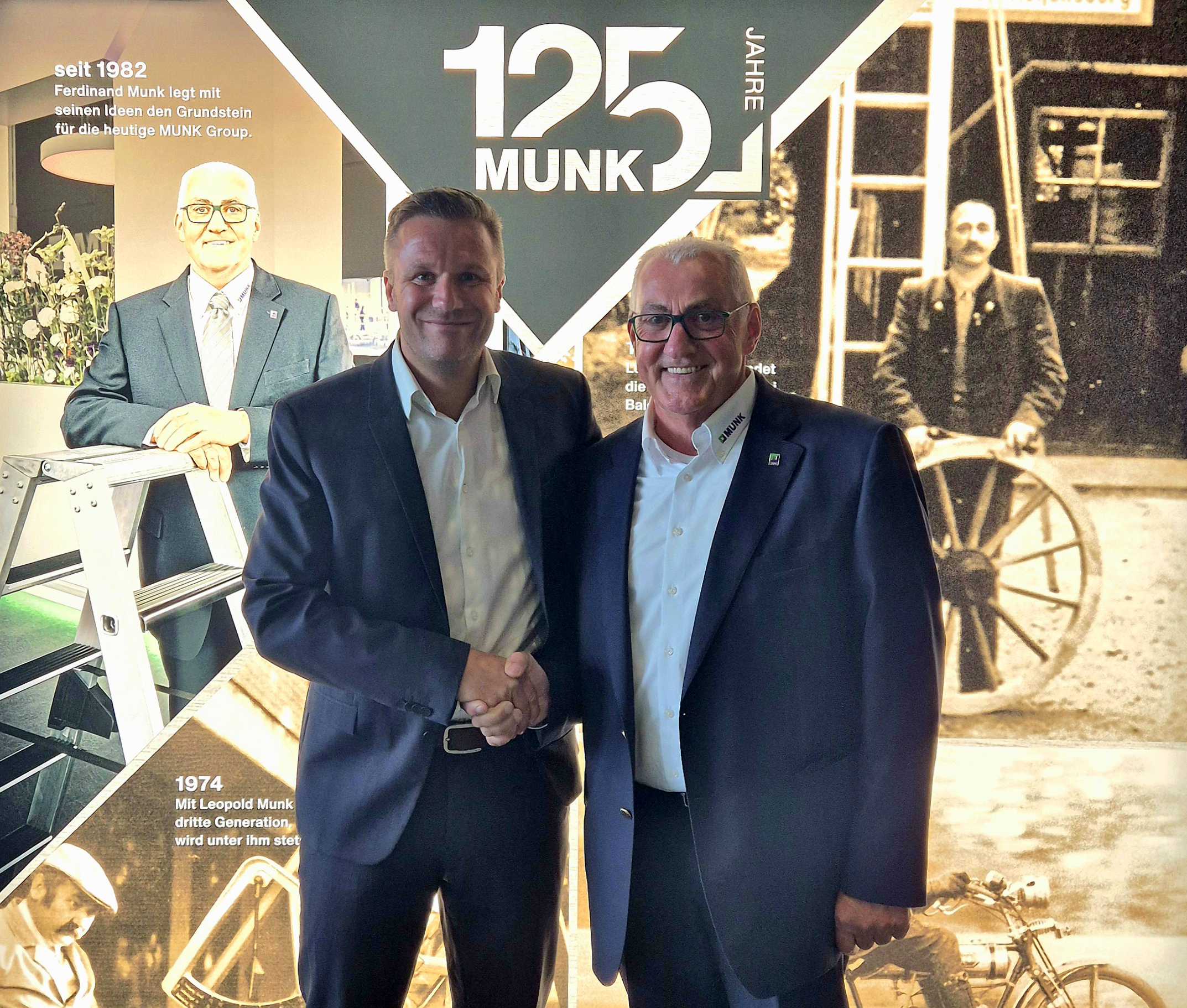 Händeschütteln vor einer Jubiläumswand: Jan Iffert und Ferdinand Munk vor einer Collage zum 125-jährigen Jubiläum der MUNK Group mit historischen und aktuellen Bildern des Unternehmens.