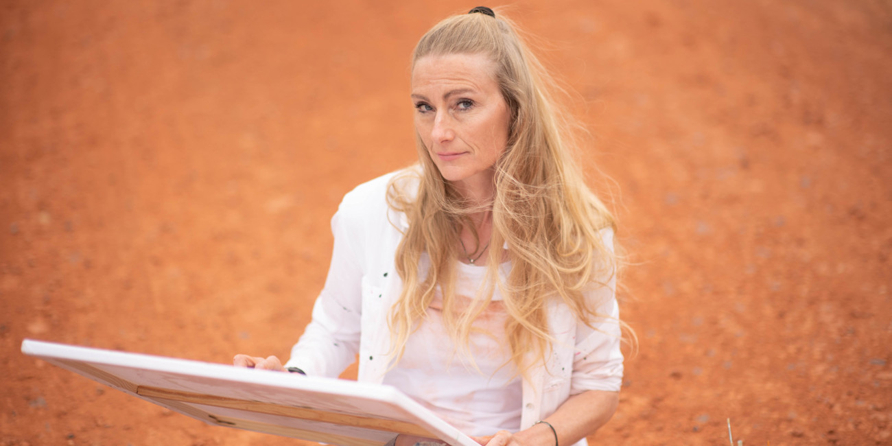 Stefanie Rau zeichnet auf einer Leinwand und blickt in die Kamera.