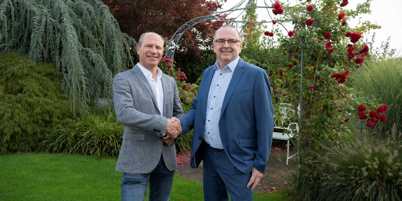 Jürgen Wohlhüter und PrivateBanking Berater Alwin Renner reichen sich im Garten partnerschaftlich die Hand.