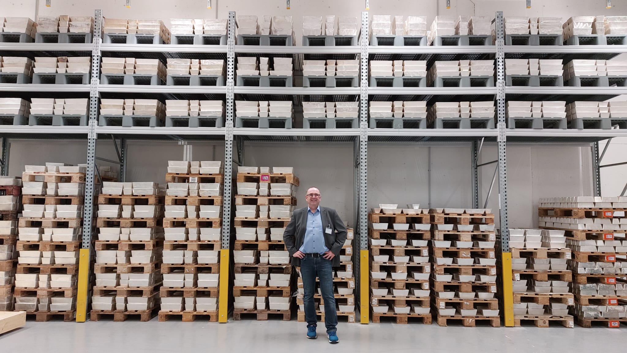 Berater Private Banking Alwin Renner steht vor einem Hochregal im Wertelager, im Regal befinden sich unterschiedliche Barren auf Paletten.